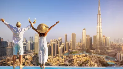 A happy tourist couple on vacation time stands by the pool edge and enjoys the panoramic sunset view of the Dubai city skyline, UAE / Foto: Shansche, Getty Images