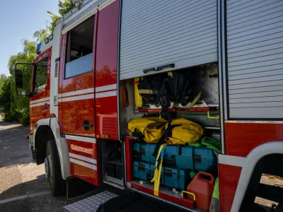 Close-up view of fire truck's open storage compartment revealing organized emergency rescue gear, colorful equipment, and yellow hoses under natural daylight conditions.