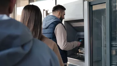 Young man using cash machine for money withdrawal outdoors. ATM queue