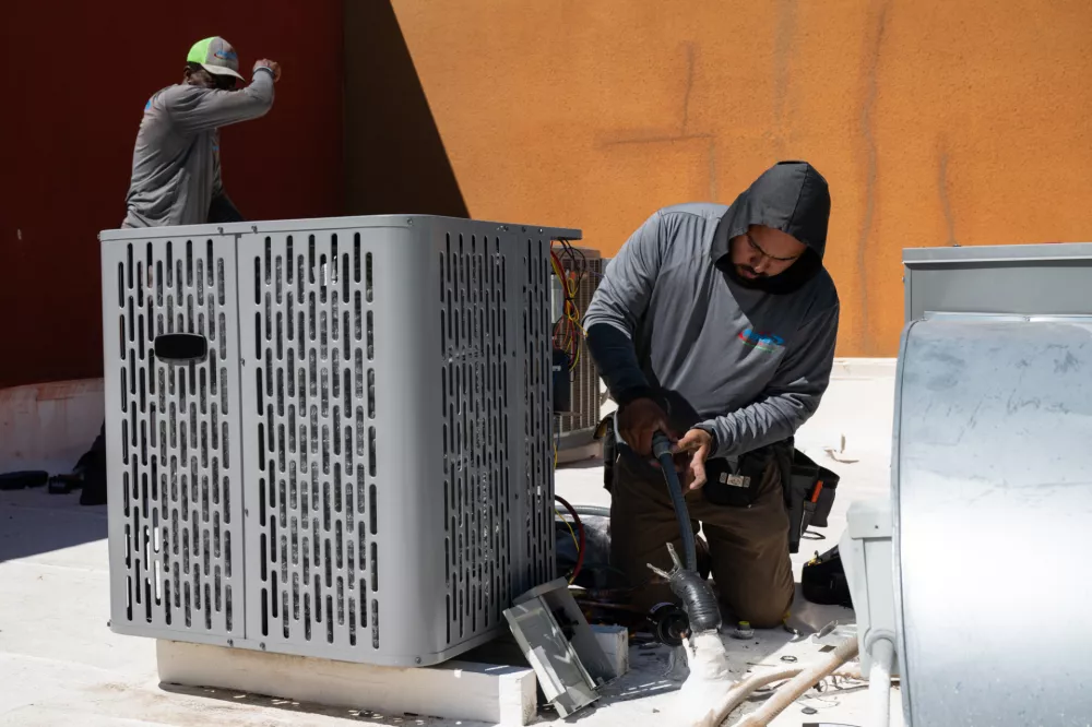 Sonel Telemaque, left, wipes sweat from his brow while installing a new air conditioning unit alongside Brian Hermosillo during record-breaking heat Thursday, March 19, 2026, in Tempe, Ariz. (AP Photo/Caitlin O'Hara)