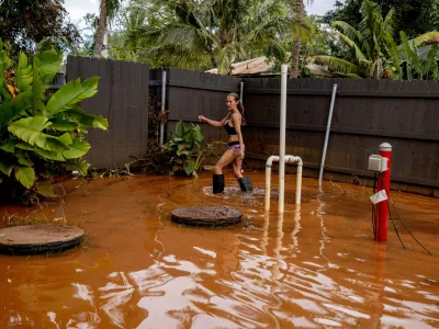 Linda Griffith wades through a flooded yard in Haleiwa, Hawaii Saturday, March 21, 2026. (Stephen Lam/San Francisco Chronicle via AP)