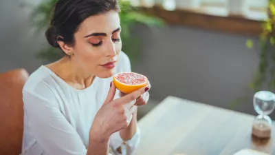 Sick woman trying to sense smell of half fresh orange, has symptoms of Covid-19, corona virus infection - loss of smell and taste. One of the main signs of the disease.
