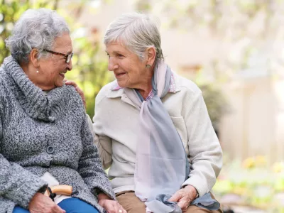 Two elderly women sitting on bench in park smiling happy life long friends enjoying retirement