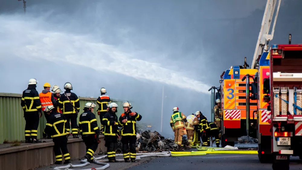 25 August 2025, Hamburg: Firefighters try to extinguish a fire in an industrial area in the port of Hamburg. A fire has broken out in a warehouse in the Port of Hamburg, causing a major motorway nearby to be closed. Photo: Daniel Bockwoldt/dpa