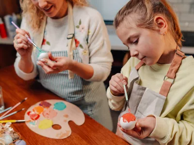 Mother and daughter sharing joyful moments, painting and decorating vibrant easter eggs with colorful paints in their cozy kitchen, creating cherished holiday memories together