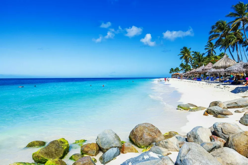 Aruba. Oranjestad. September 12.2022. Beautiful view of Eagle Beach with white sand, turquoise Caribbean Sea, people swimming and palm trees with straw umbrellas. / Foto: Alexander Shapovalov