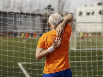 Rear view of senior sportsman standing on stadium and stretching his arms.