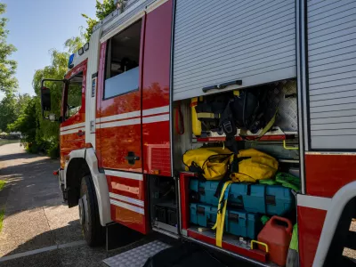 Close-up view of fire truck's open storage compartment revealing organized emergency rescue gear, colorful equipment, and yellow hoses under natural daylight conditions.