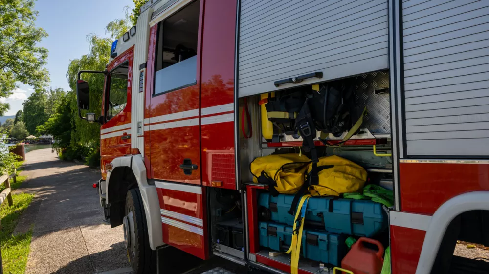 Close-up view of fire truck's open storage compartment revealing organized emergency rescue gear, colorful equipment, and yellow hoses under natural daylight conditions.