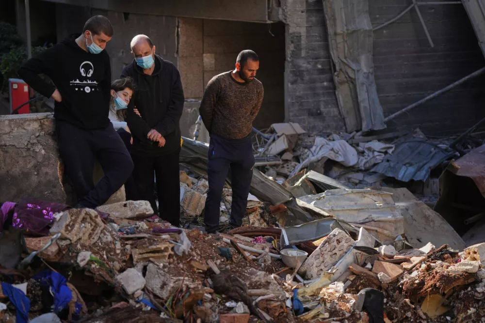 Residents Omar Amouri, second right, and his daughter Lara stand amid debris with others at the site of a building where efforts continue to recover the body of missing woman Zahraa Aboud, 26, after it was destroyed in an Israeli airstrike on Wednesday, in central Beirut, Sunday, April 12, 2026. (AP Photo/Hassan Ammar)
