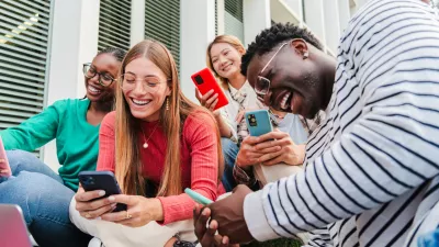 Group of smiling young multiethnic high school students using cellphones. Guys and females watching social media with their smartphones, while enjoying together sitting at the university campus lawn. High quality photo