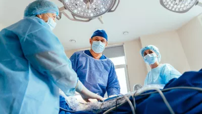 Low angle portrait of experienced male surgical and team making operation in sterile medical room. Two female assistants help him. Minimally invasive surgery. / Foto: Iryna Inshyna