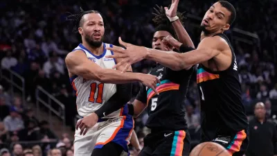 New York Knicks' Jalen Brunson, left, passes around San Antonio Spurs' Victor Wembanyama, right, and Stephon Castle during the first half of an NBA basketball game Sunday, March 1, 2026, in New York. (AP Photo/Seth Wenig)