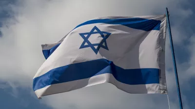 The flag of Israel against a blue sky with white clouds on a sunny day.